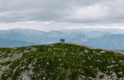 Drei wandernde Personen stehen auf einem Wanderweg entlang eines Kamms, dahinter die Berglandschaft.