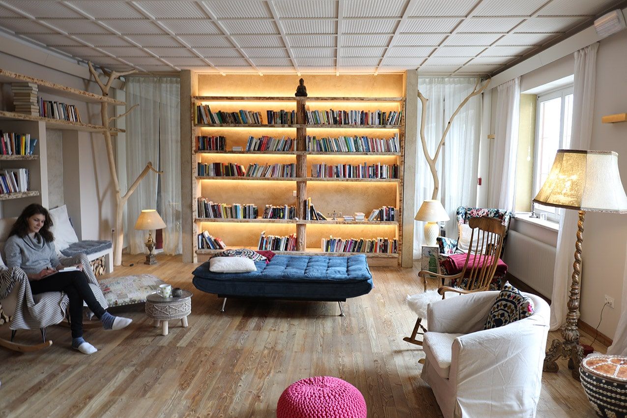 Cozy library with a large, illuminated bookshelf, armchairs and a person reading.