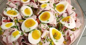 A plate with sausage salad, boiled eggs and chives.