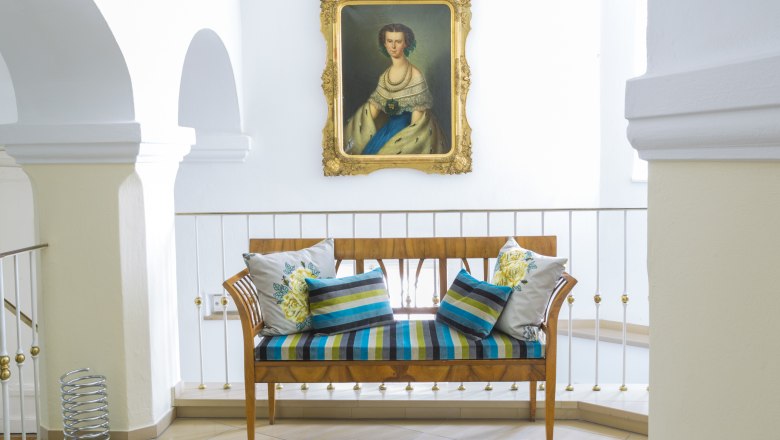 Elegant bench with colorful cushions in front of a painting in a bright room.