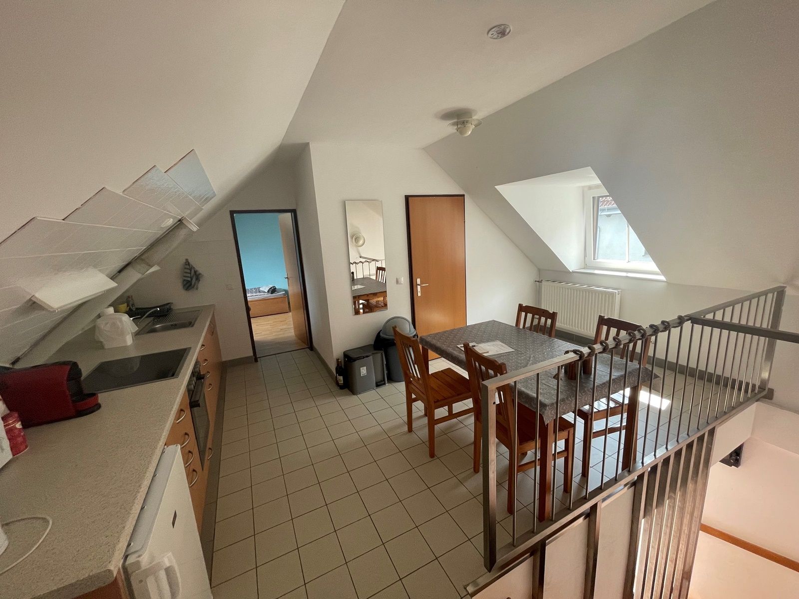 Kitchen-cum-living room with dining table, chairs, kitchenette and sloping roof.