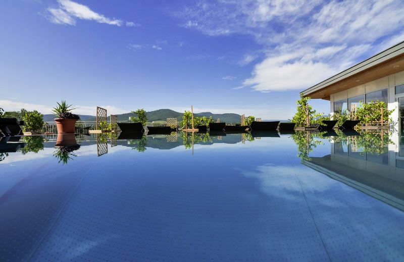 A modern pool on a penthouse with a view of the mountains and blue sky.