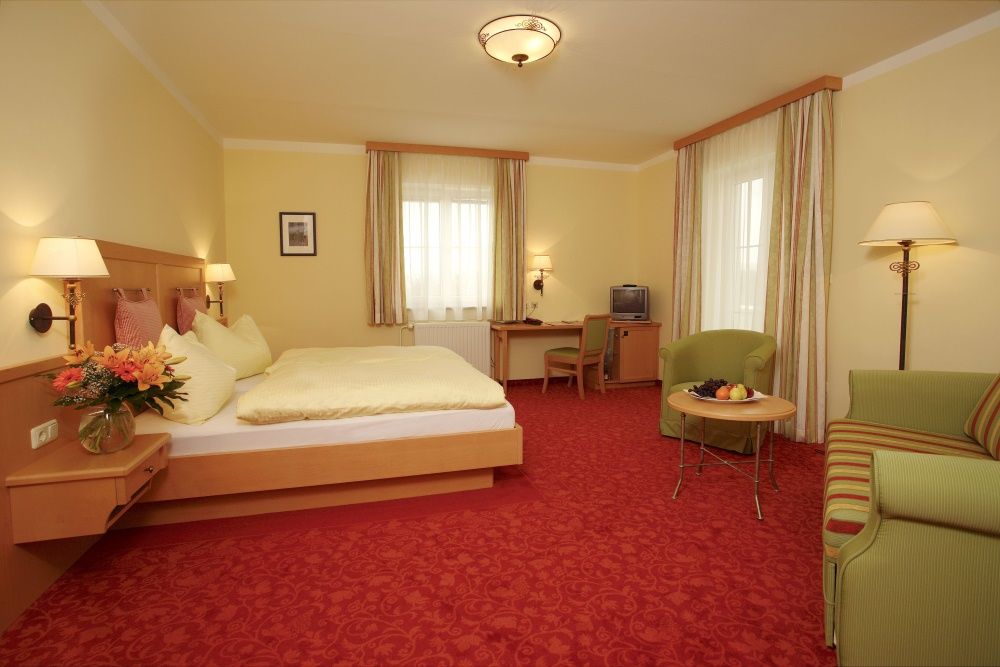 A cozy hotel room with a double bed, sofa, table and TV. Yellow walls and red carpets dominate the room.