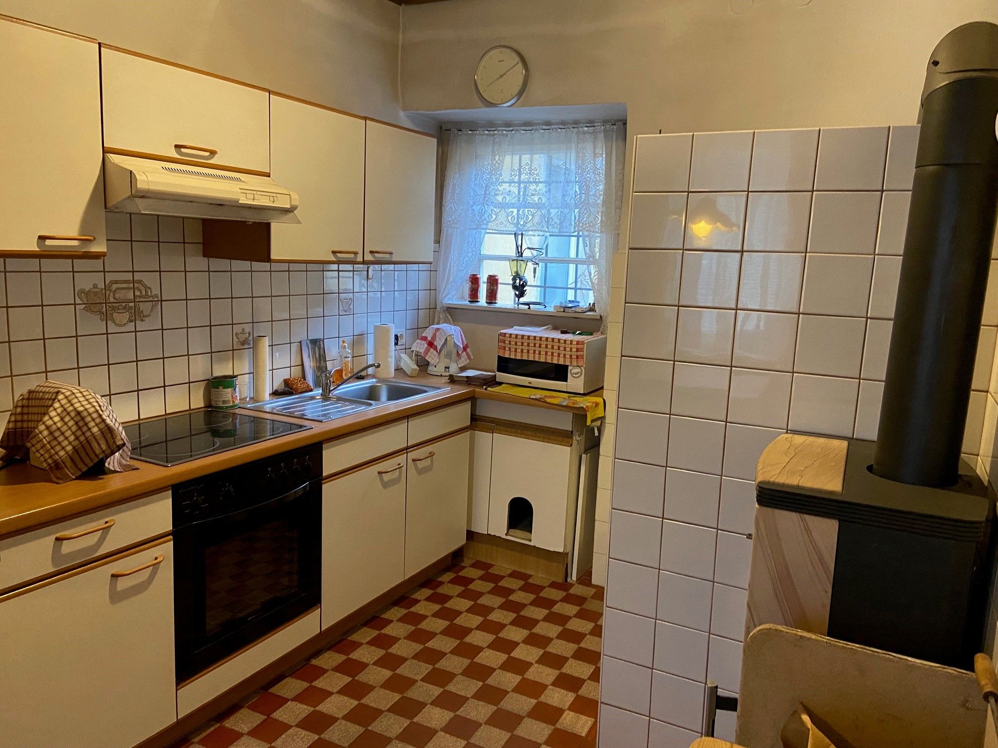 Kitchen with white cupboards, stove, sink and wood-burning stove.