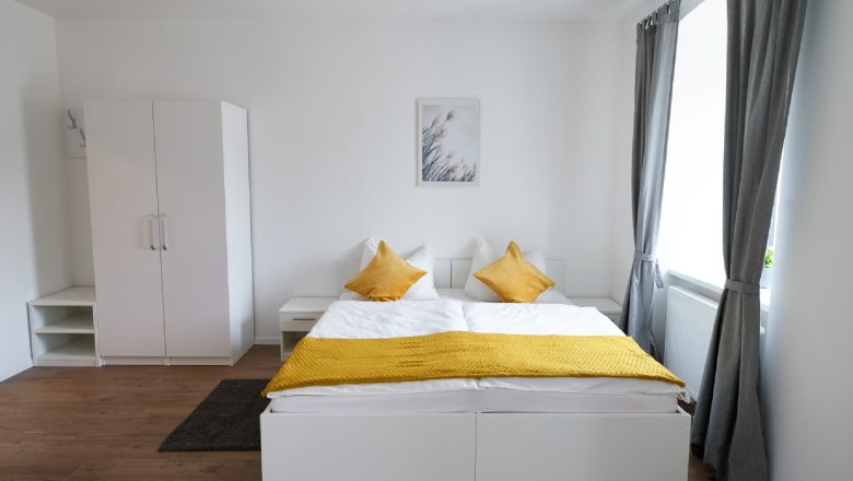 Modern double room with white bed, yellow pillows and gray curtains.