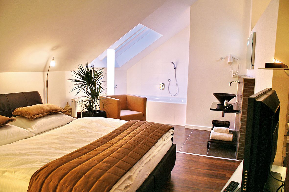 Cozy bedroom with double bed, plants, armchair and bathtub under a sloping roof.