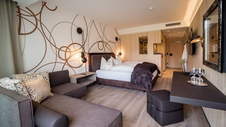 Modernly furnished hotel room with double bed, sofa and desk.