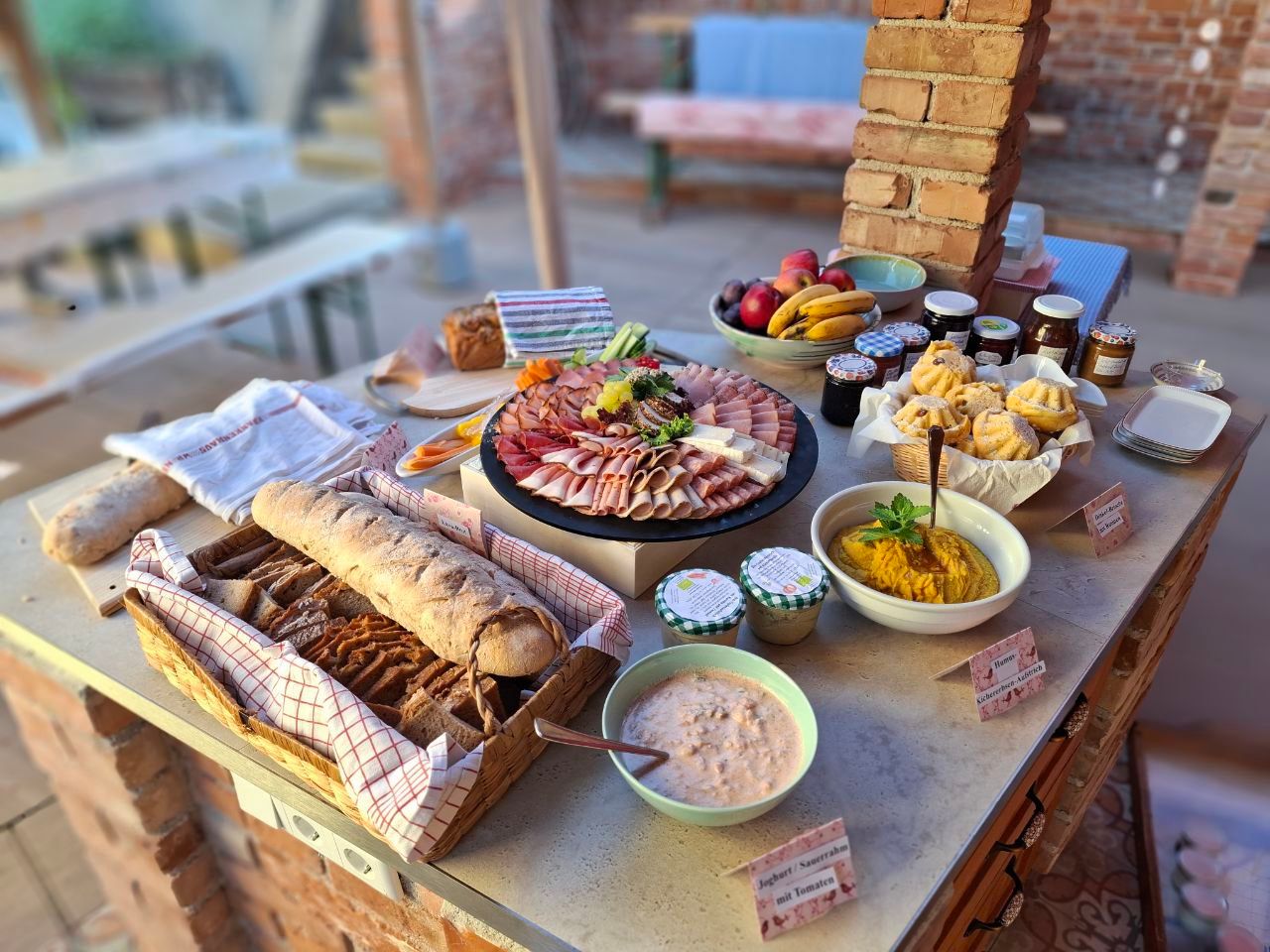 A buffet with bread, cold cuts, fruit, jams and dips on a table.