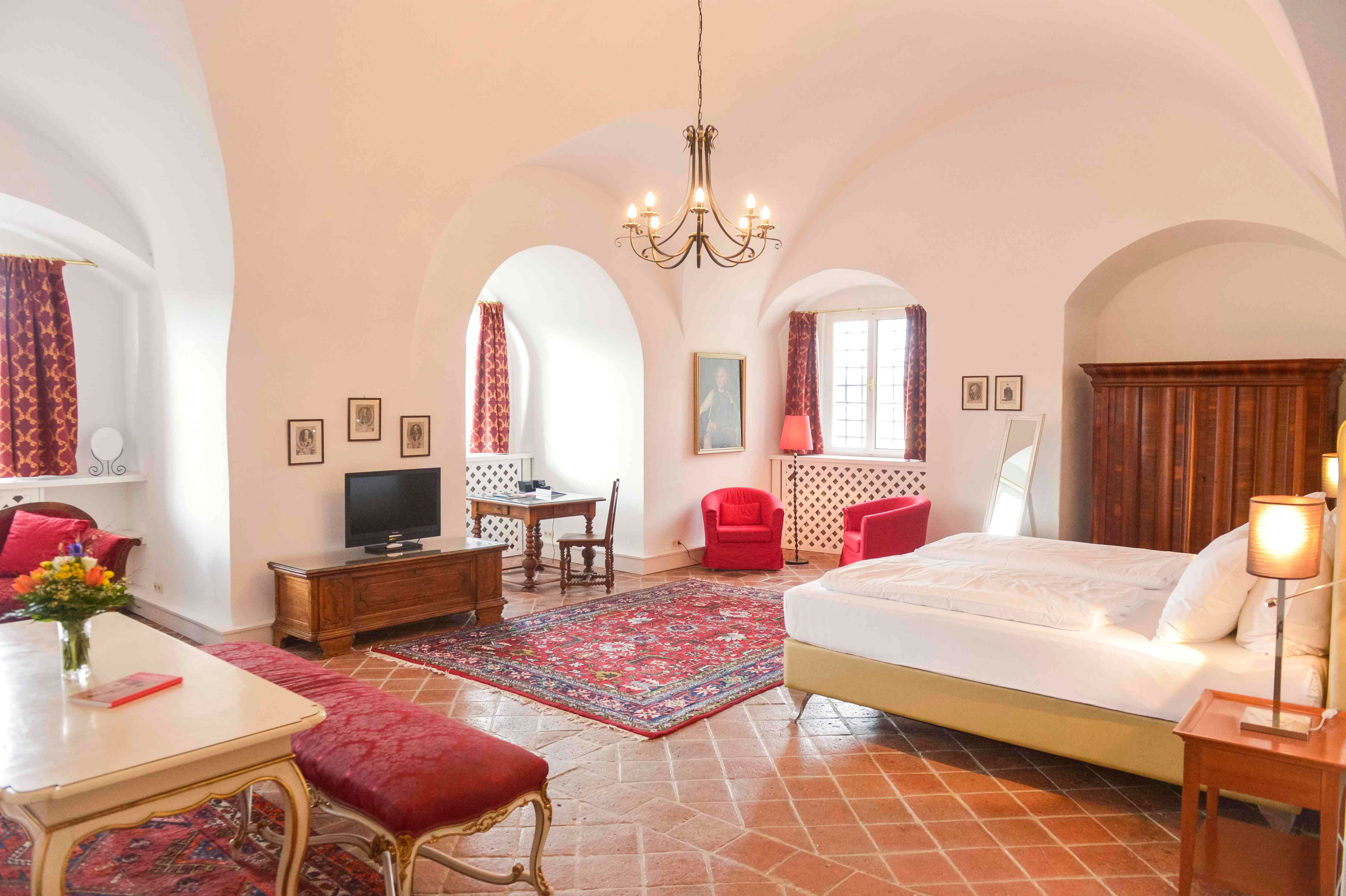 Luxurious suite with antique furniture, red carpets and curtains, a large bed and a chandelier.