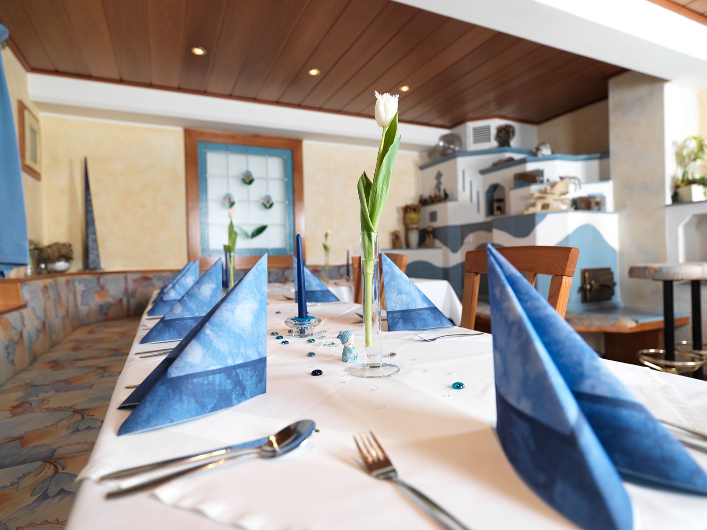 An elegantly laid table with blue napkins and a white tulip in a glass in a cozy room.