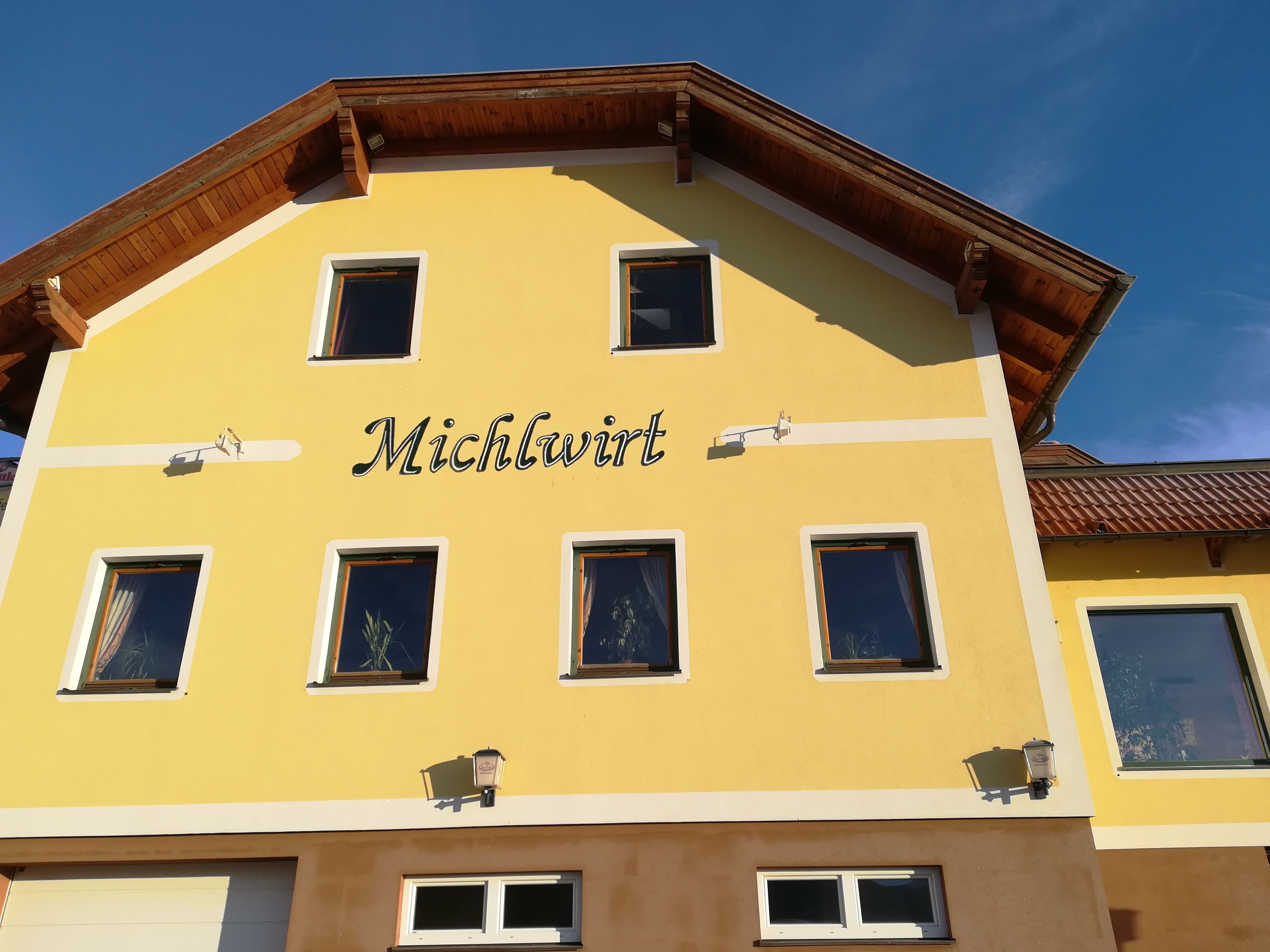 Yellow building with the inscription 'Michlwirt' and several windows, under a blue sky.