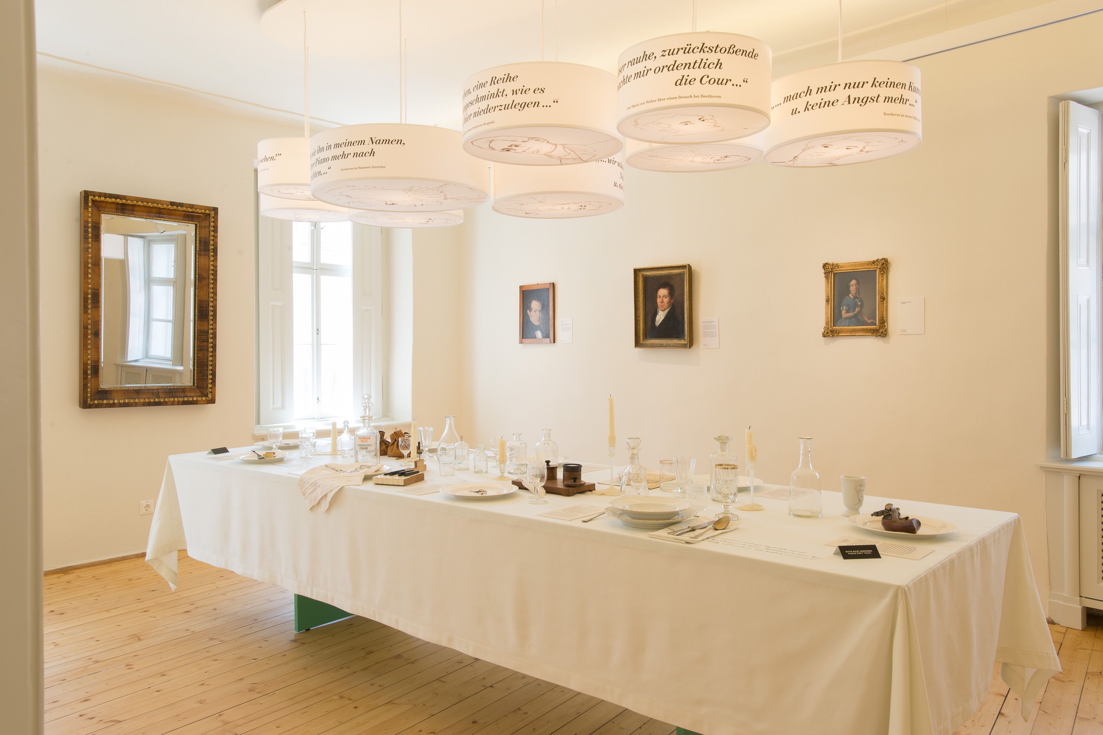 A laid table in a room with portraits on the wall and hanging lamps with texts.