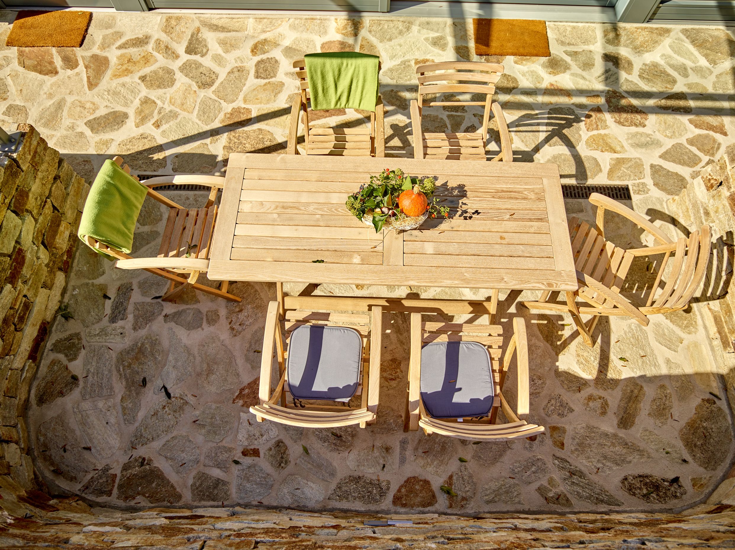 Wooden table with chairs on a stone terrace, decorated with pumpkins and flowers.
