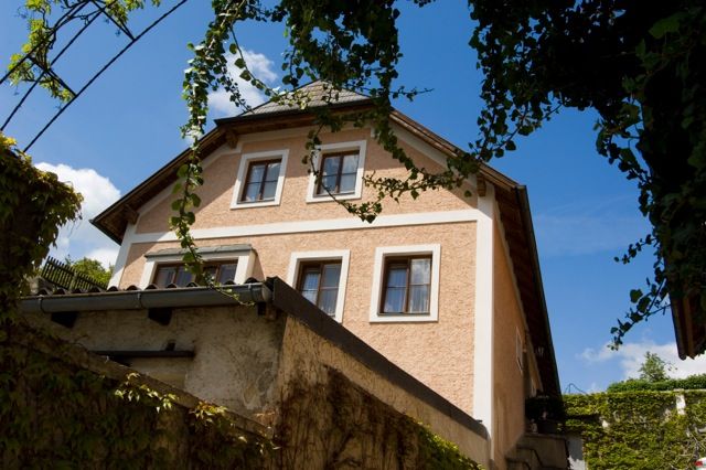 Exterior view of a traditional house overgrown with ivy, blue sky in the background.