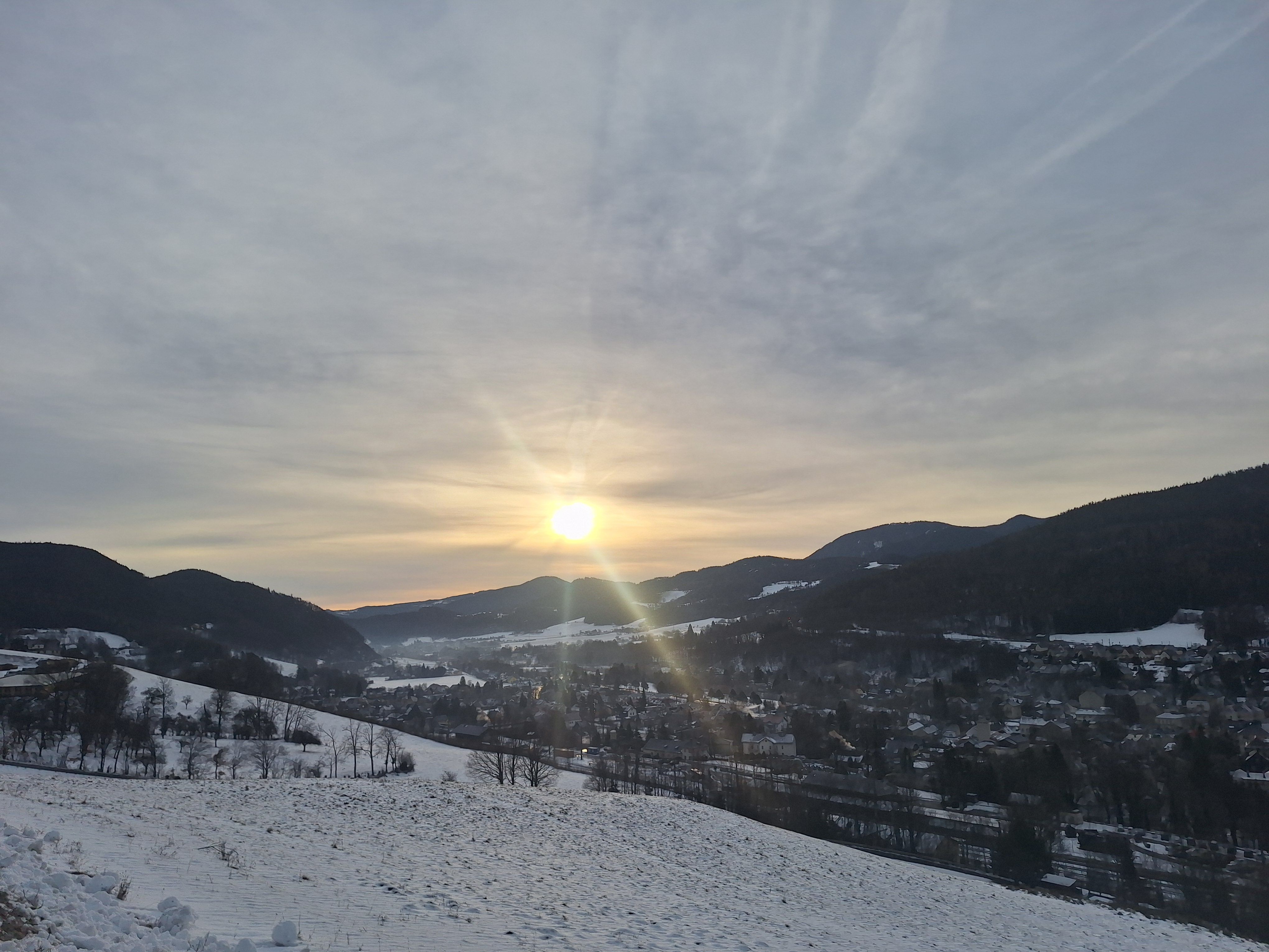 Winter landscape in Payerbach with sunrise over snow-covered hills and a village in the valley.
