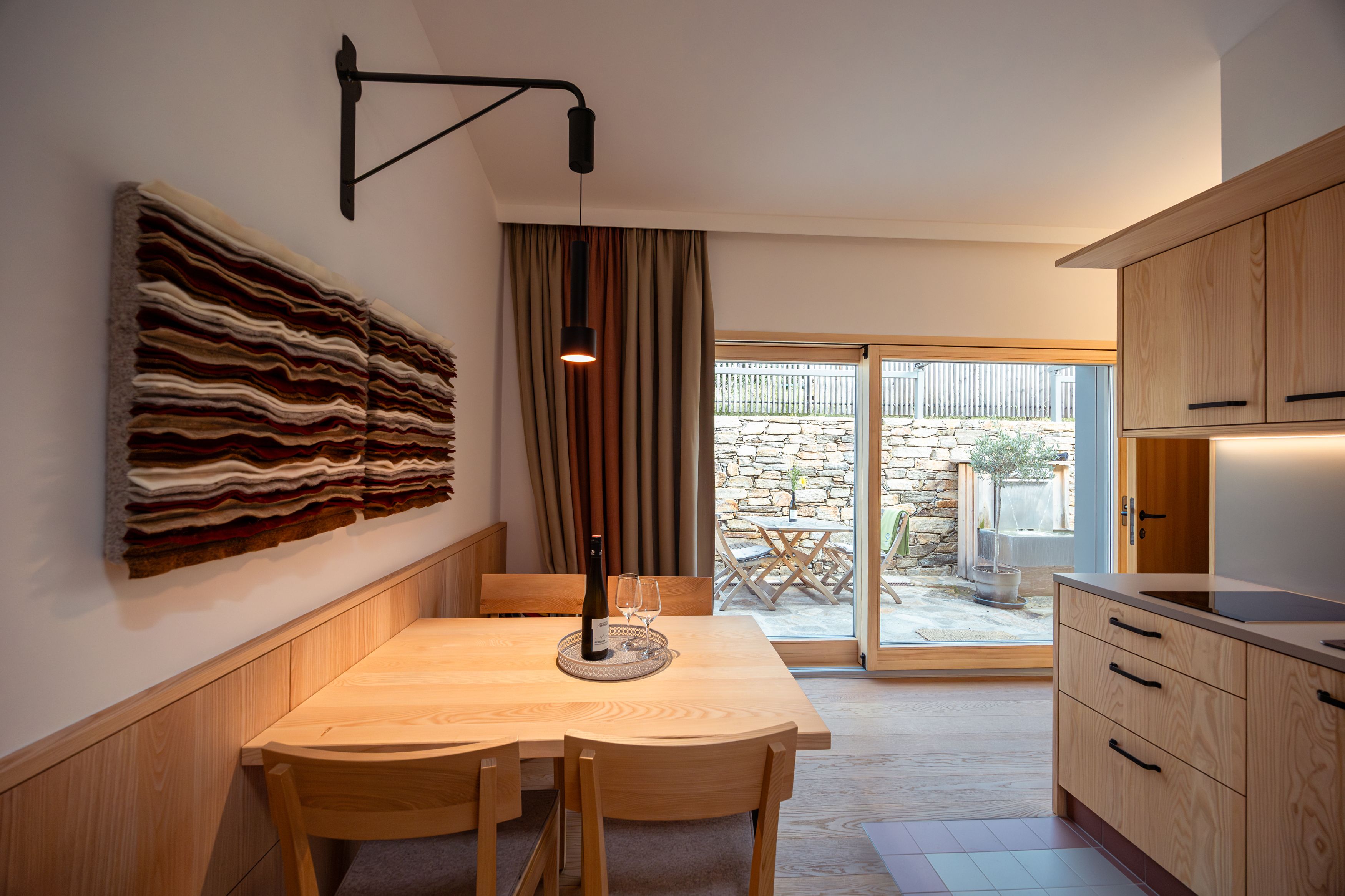 Interior view of a modern dining area with wooden furniture and wall art, view of a terrace through a glass door.