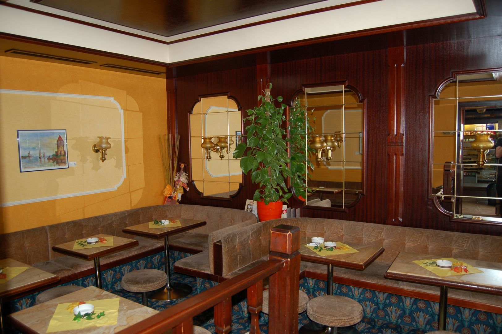 Interior view of a traditional coffee house with wooden furniture, mirrors and plants.