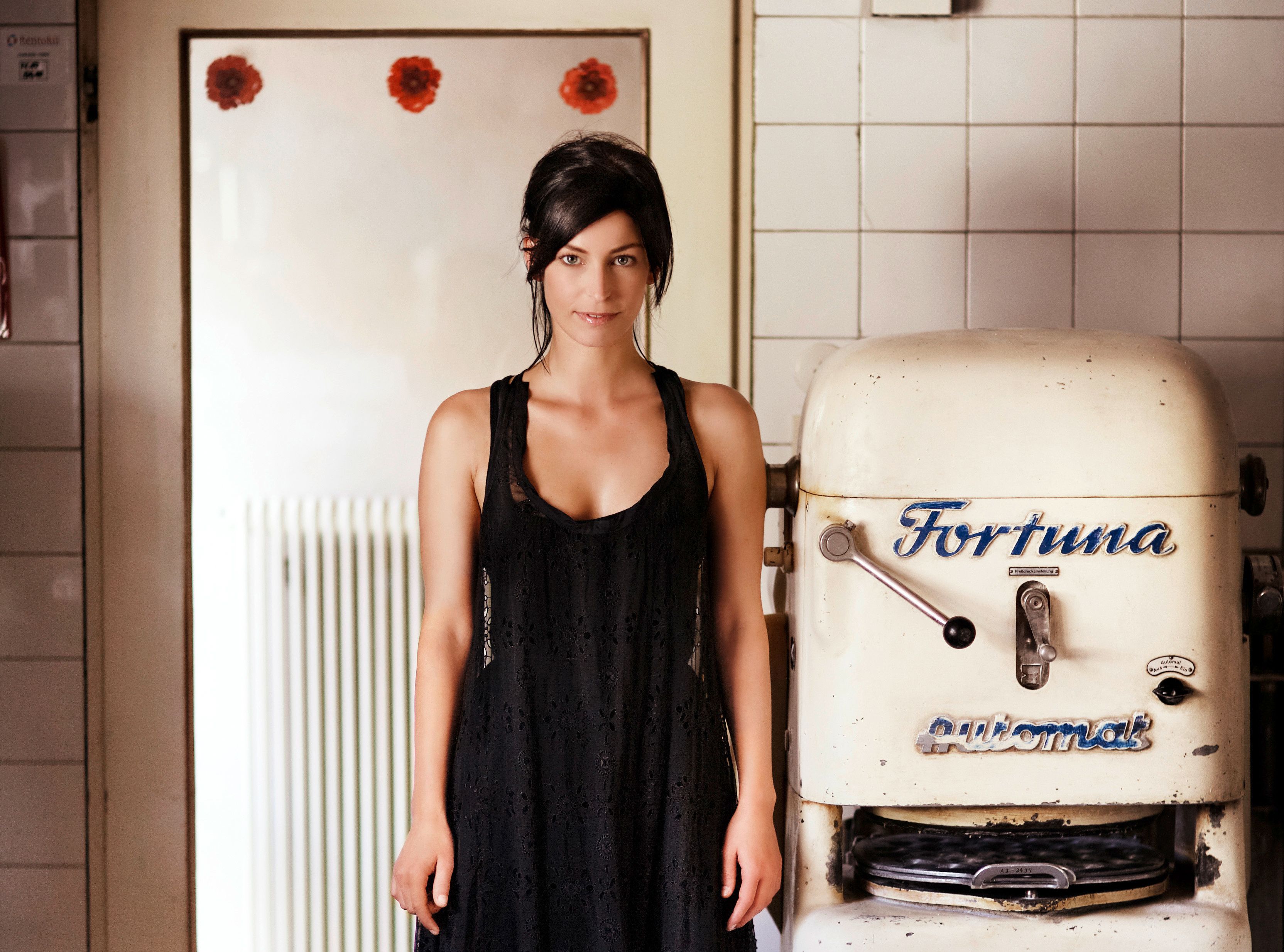 A woman in a black dress stands next to an old bakery machine labeled 'Fortuna'.