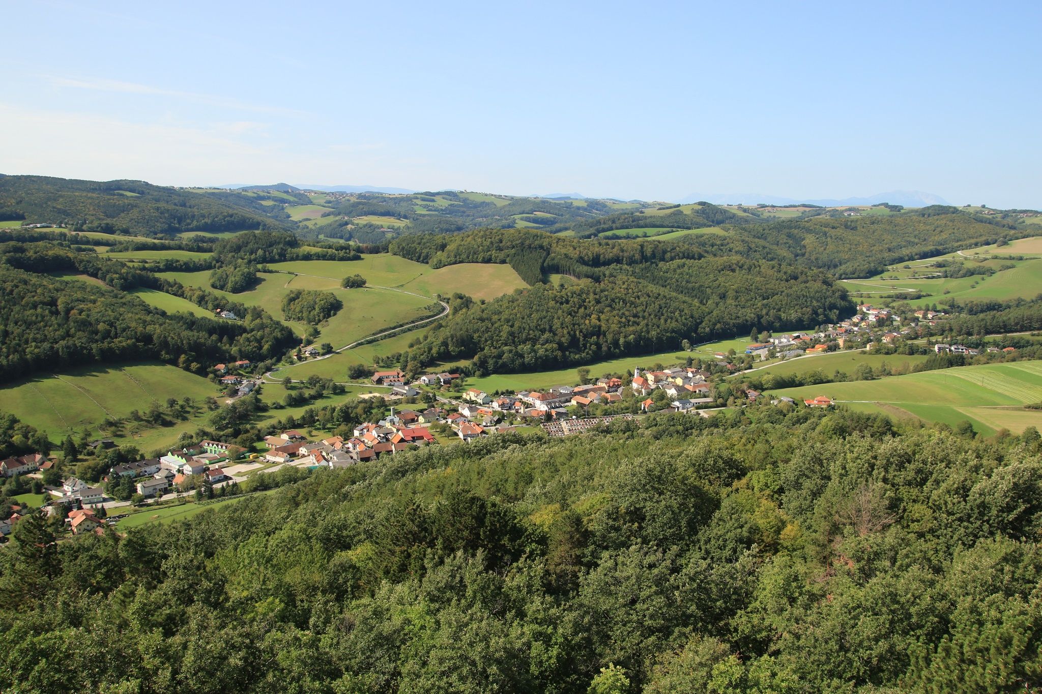 Panoramic view of a green hilly landscape with a village in the foreground, taken from the Johann Giefing observation tower.