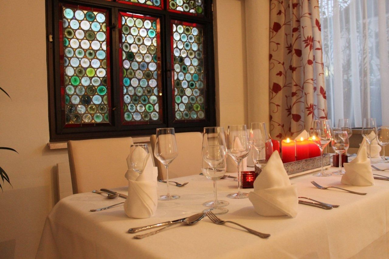 Elegant table with white tablecloths, wine glasses and red candles in front of a colorful window.