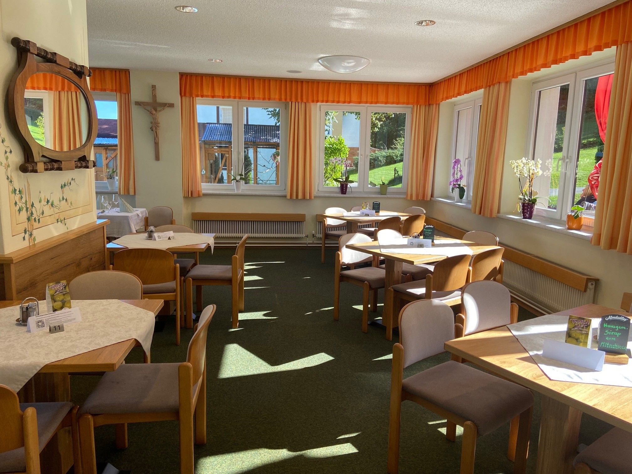 A bright dining room with wooden tables, chairs and large windows with orange curtains.