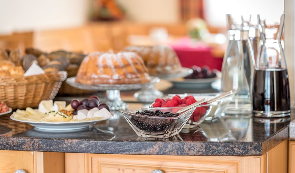 Breakfast buffet with cake, berries, cheese platter and drinks on a table.