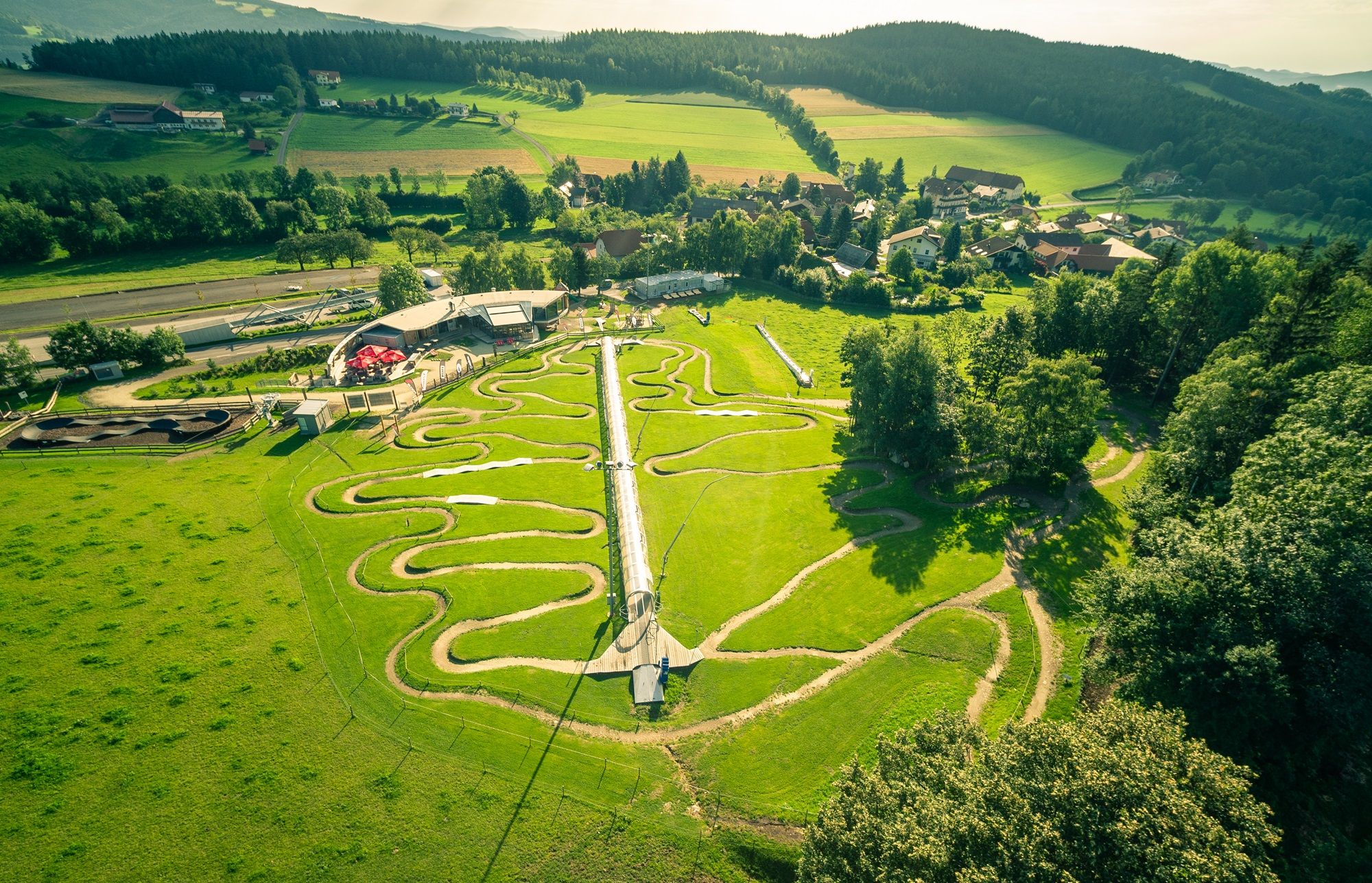 Aerial view of the Wexl Arena in St. Corona with green hills and winding paths.