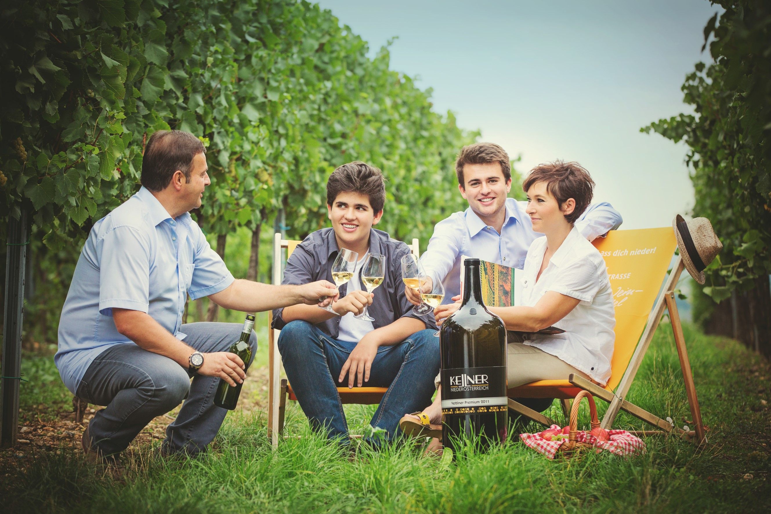 Four people sit in a vineyard and toast with wine glasses.