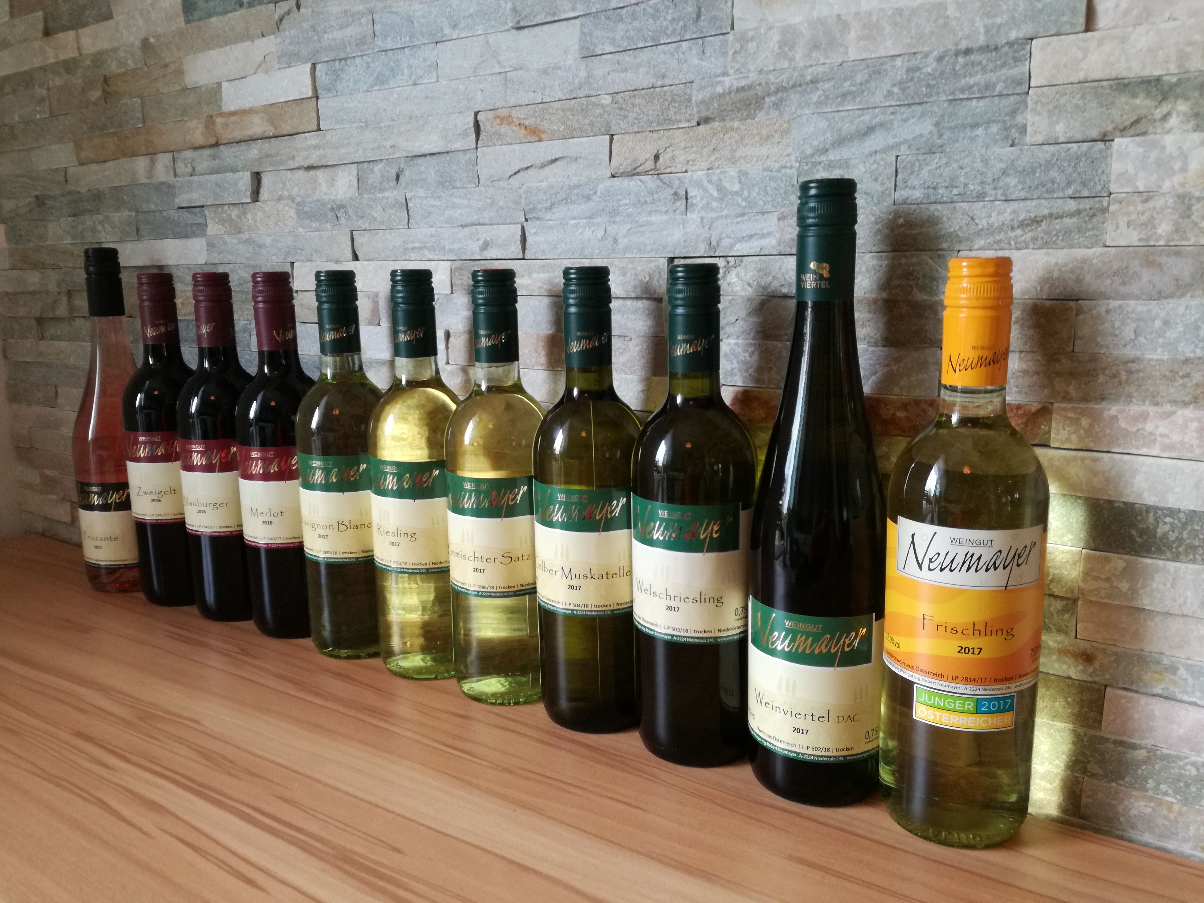A row of wine bottles from the Neumayer winery in front of a stone wall.