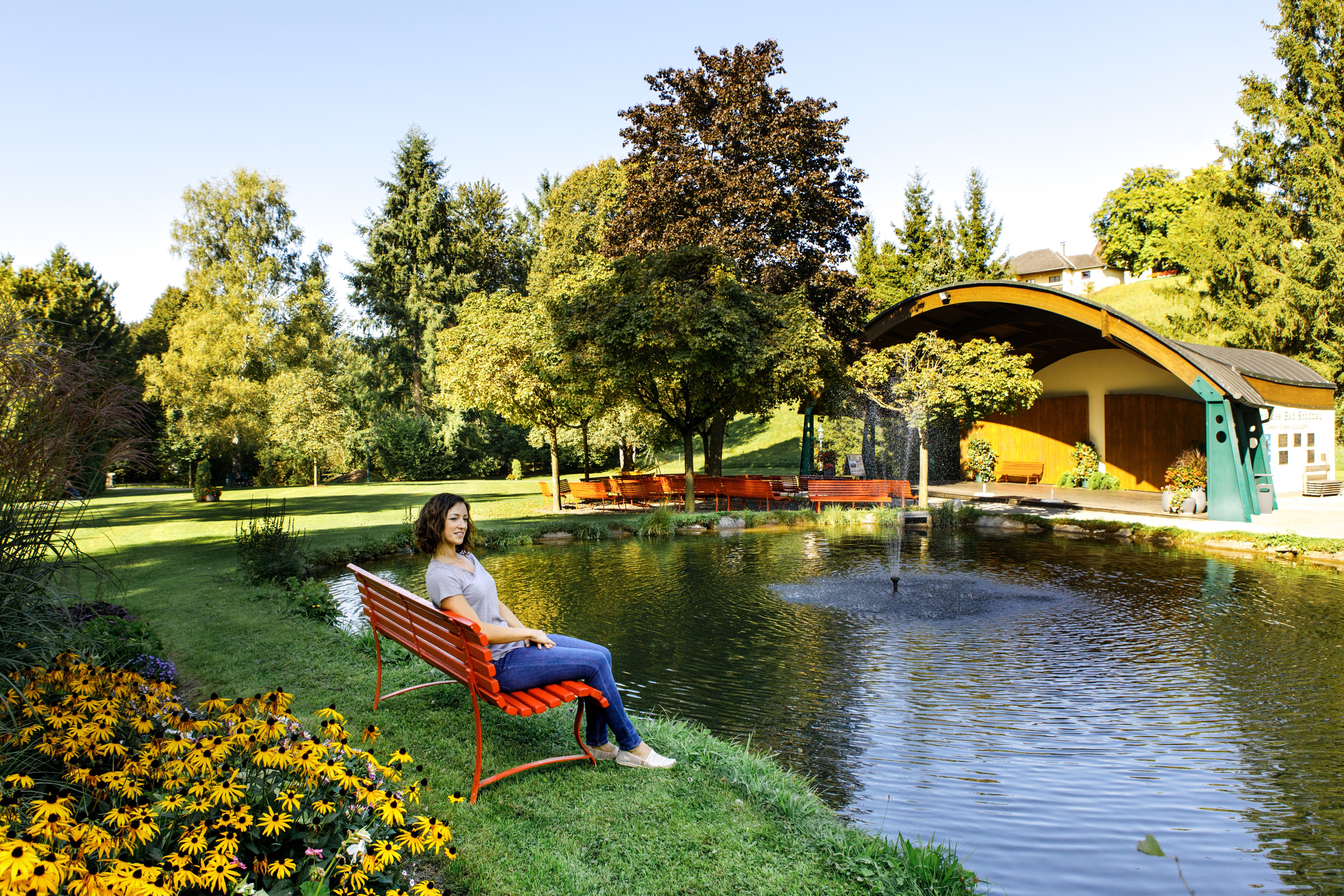 Woman sitting on a red bench by the pond in Bad Schönau spa gardens.
