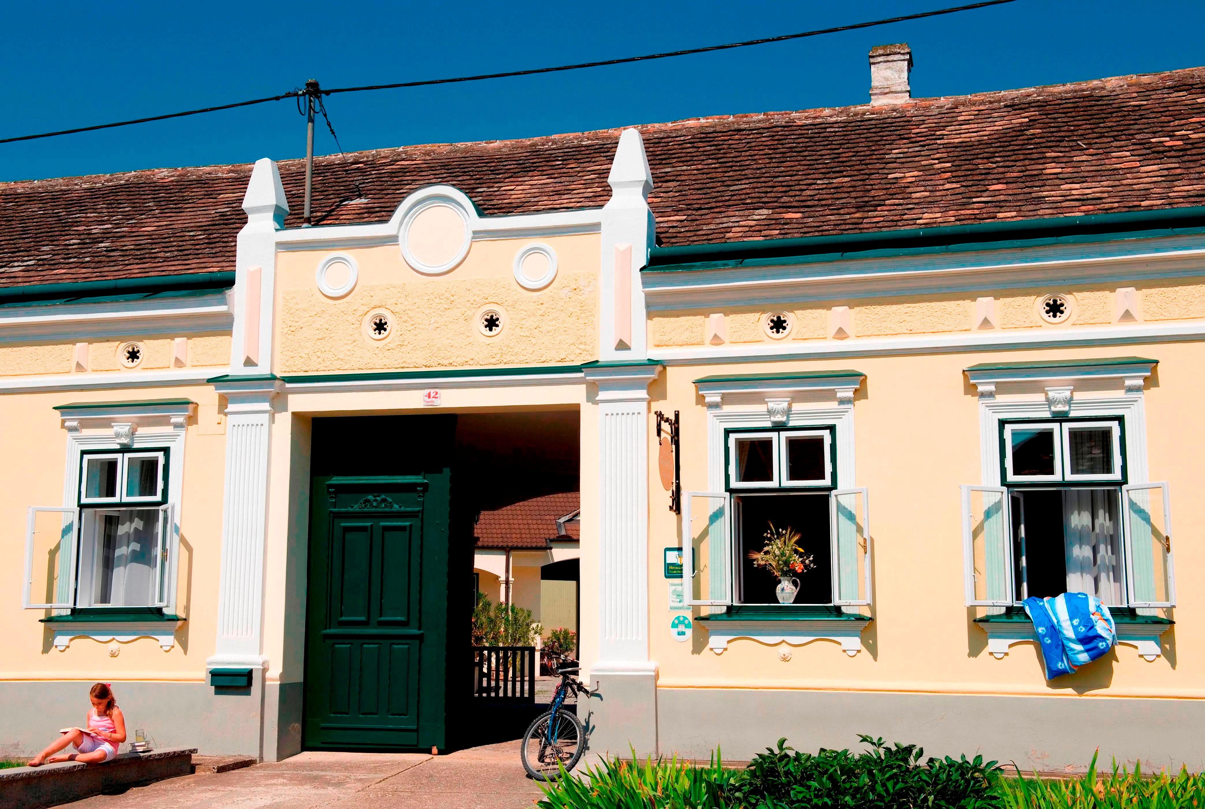 A traditional yellow building with green doors and windows, a bicycle in front of it and a child sitting on the stairs.