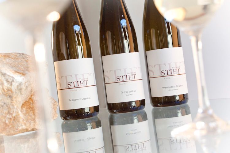 Three wine bottles of the brand Stift on a table, surrounded by wine glasses.