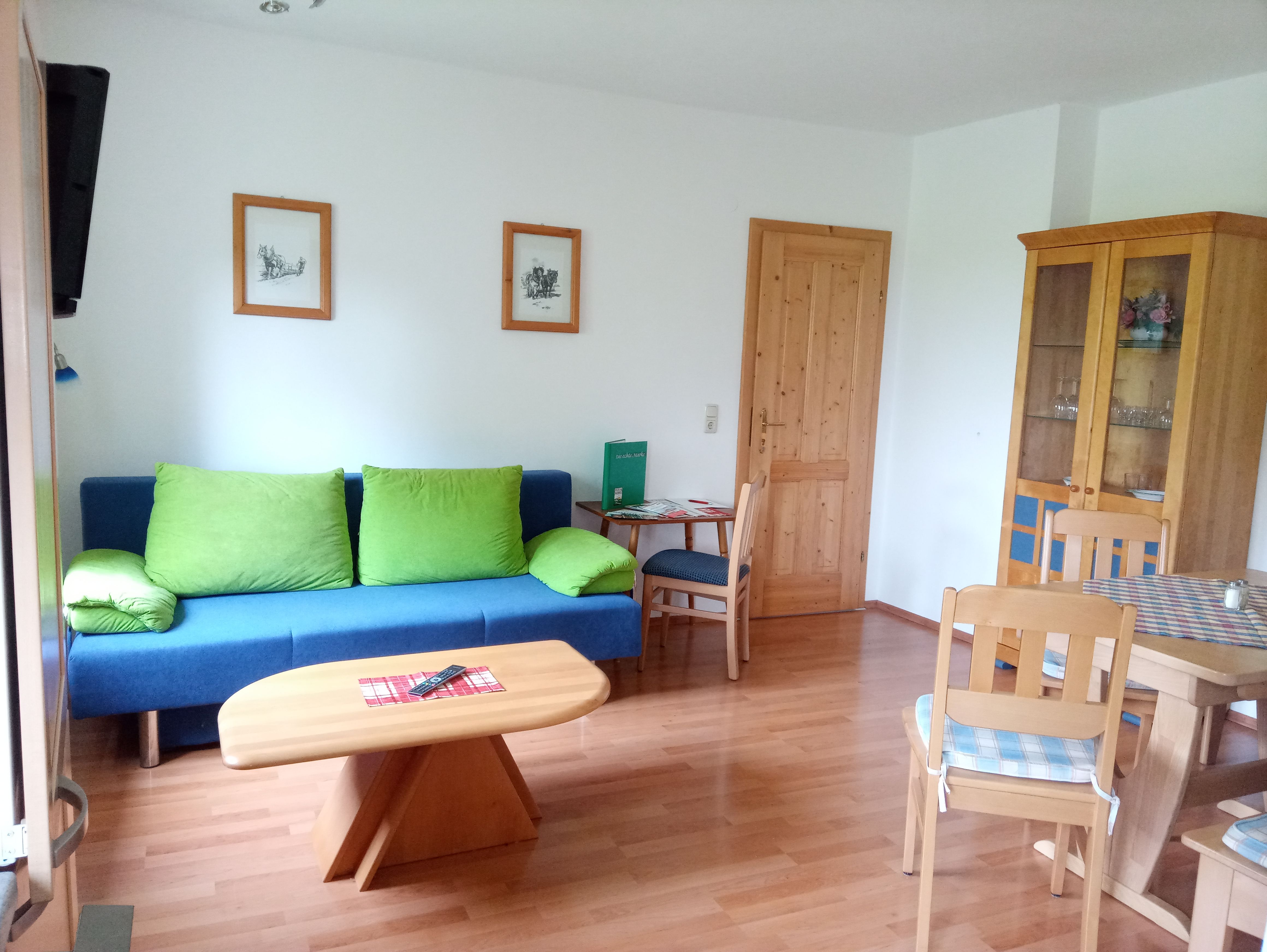 Living room with blue couch, wooden table and chairs, cupboard and pictures on the wall.