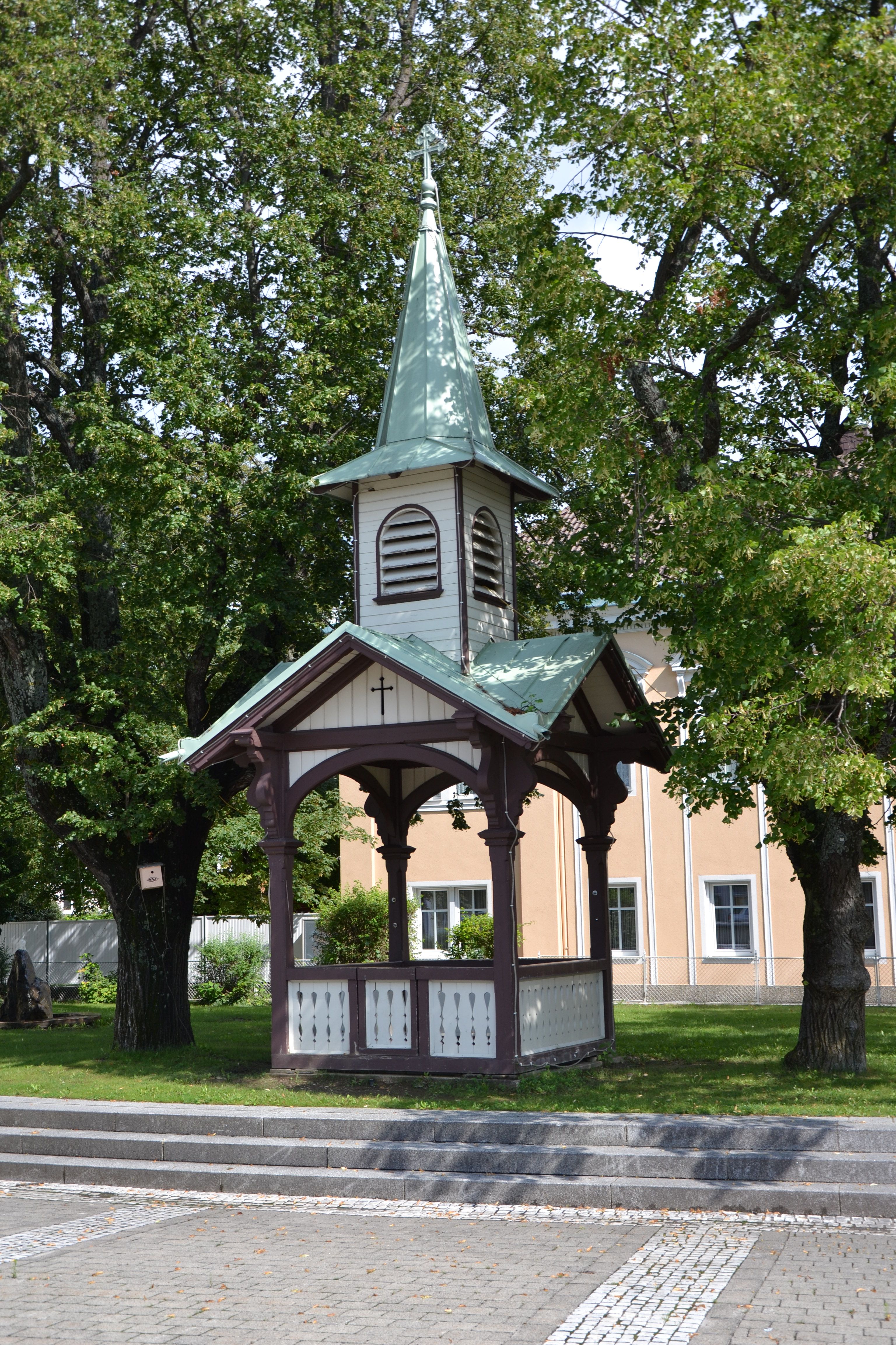 A small pavilion with a pointed roof and cross, surrounded by trees.