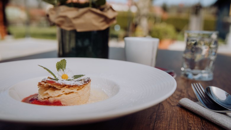 A plate of milk cream strudel, garnished with a daisy, on a wooden table outside.