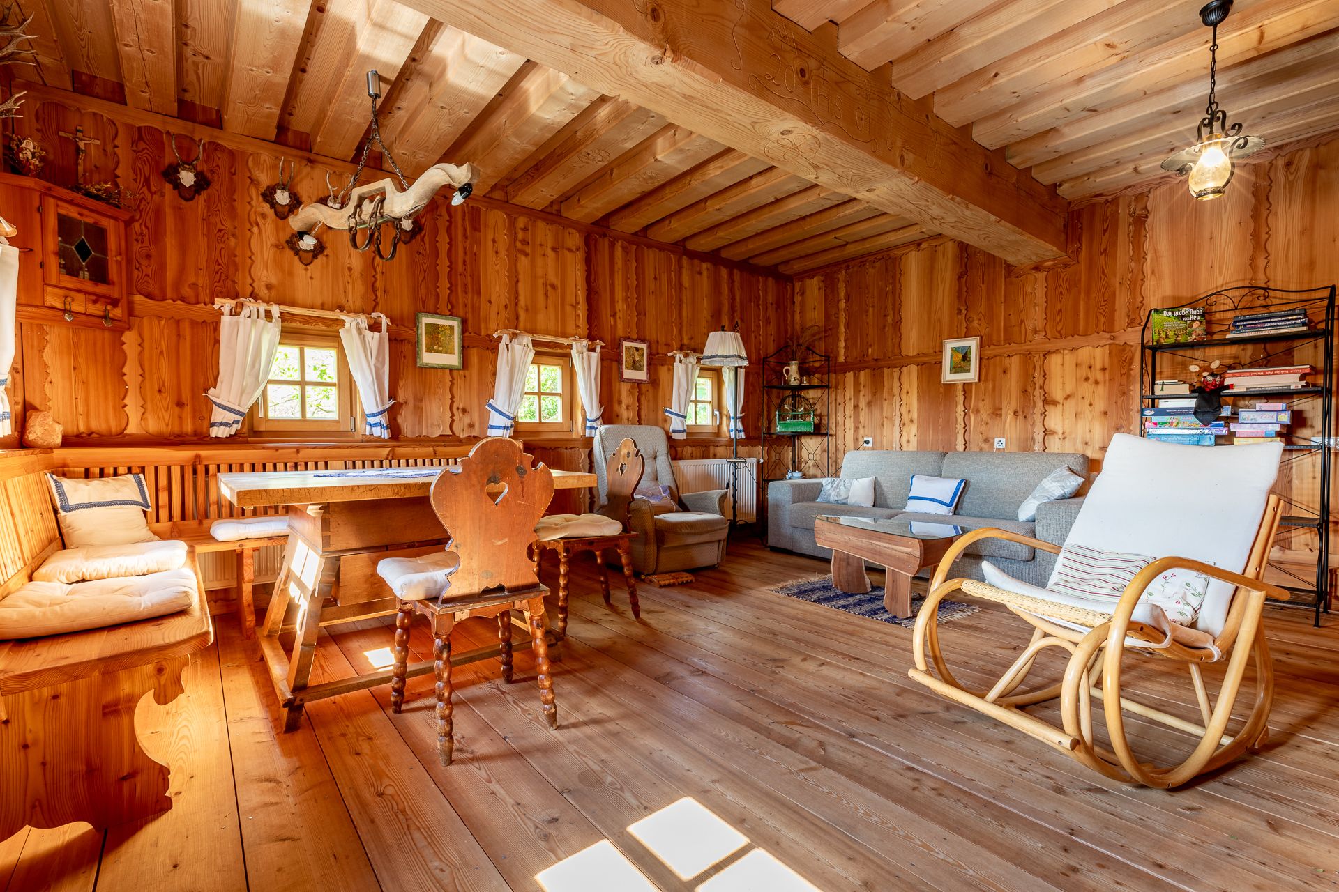 Dining area with wooden furniture, rocking chair and sofa in a room with wood paneling.