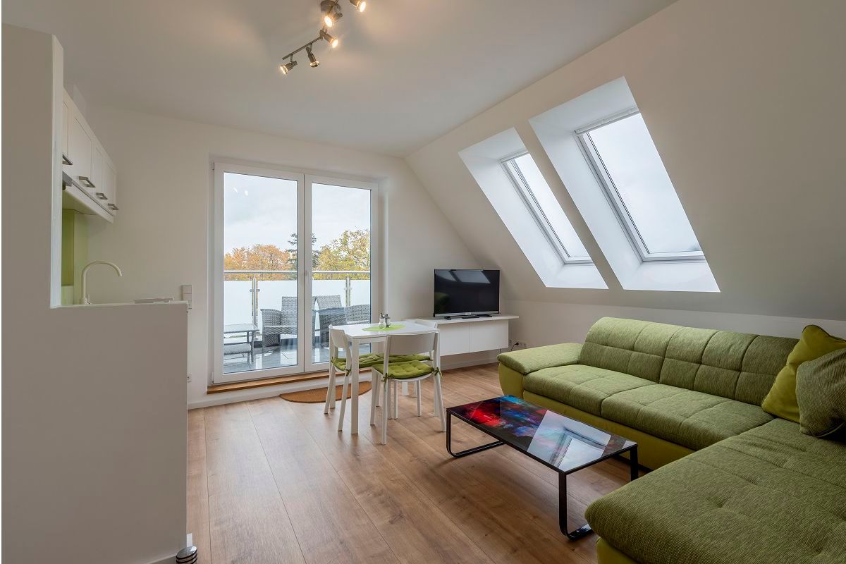 Modern living room with green couch, glass table, TV and balcony access.