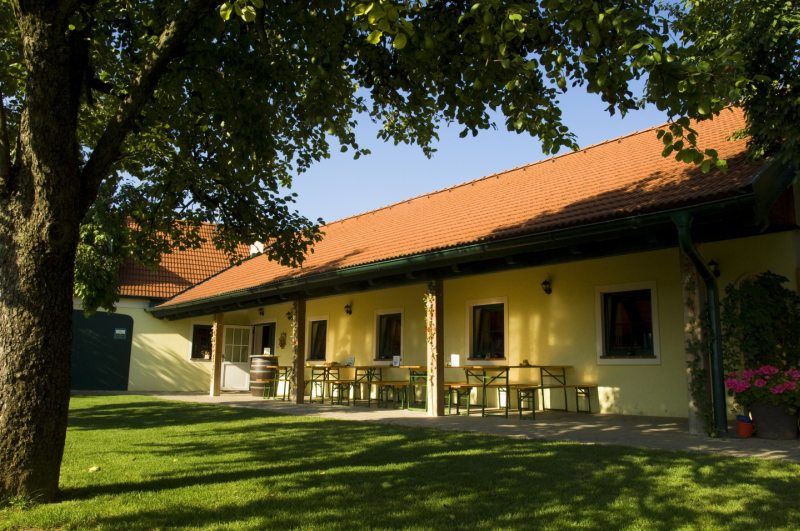 A Heurigen garden with a yellow building, red roof tiles and a green meadow.