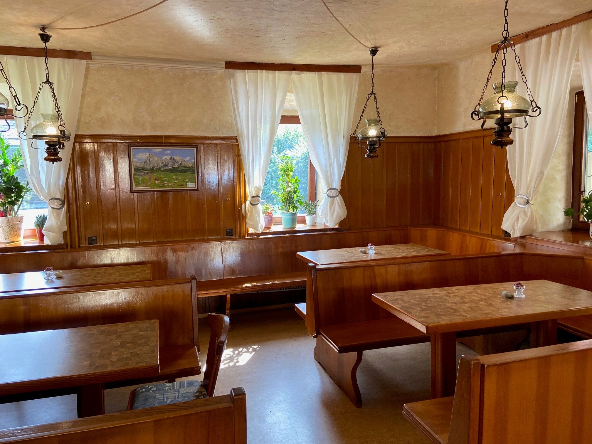 Cozy dining room with wooden furniture, white curtains and plants on the windowsill.
