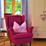 Cozy room with pink armchair, cushions, small table and wardrobe.