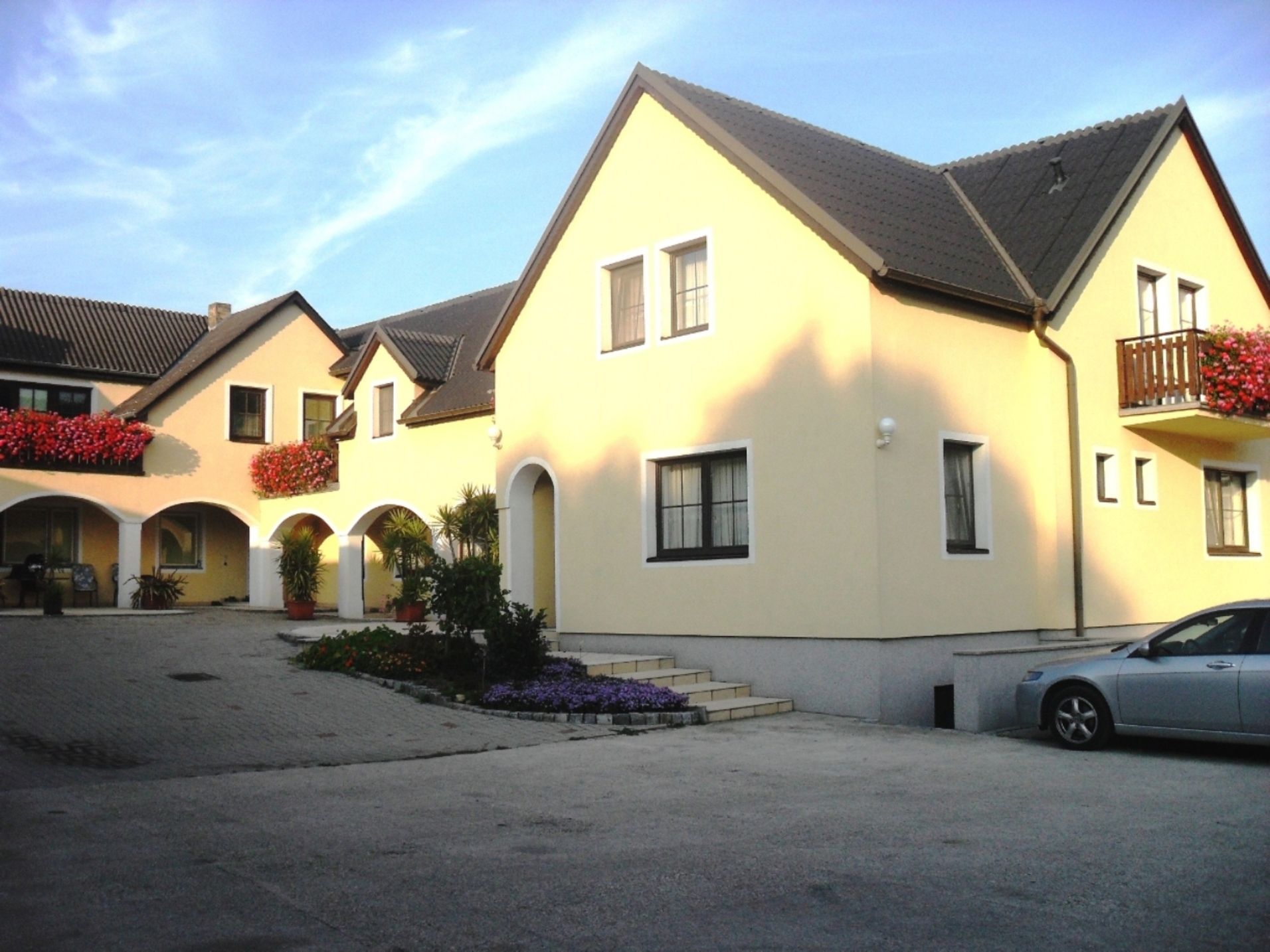 Yellow cottage with flowers and car in the yard.