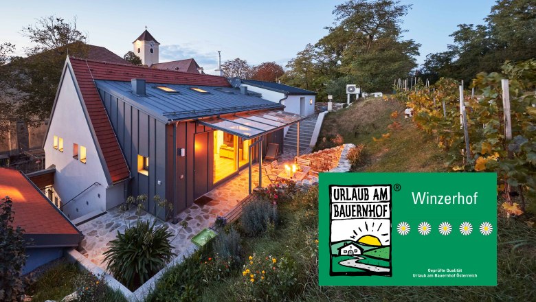A modern Kellerstöckl in the Weinviertel at dusk, surrounded by vines and a garden. A sign shows 'vacation on a farm'.