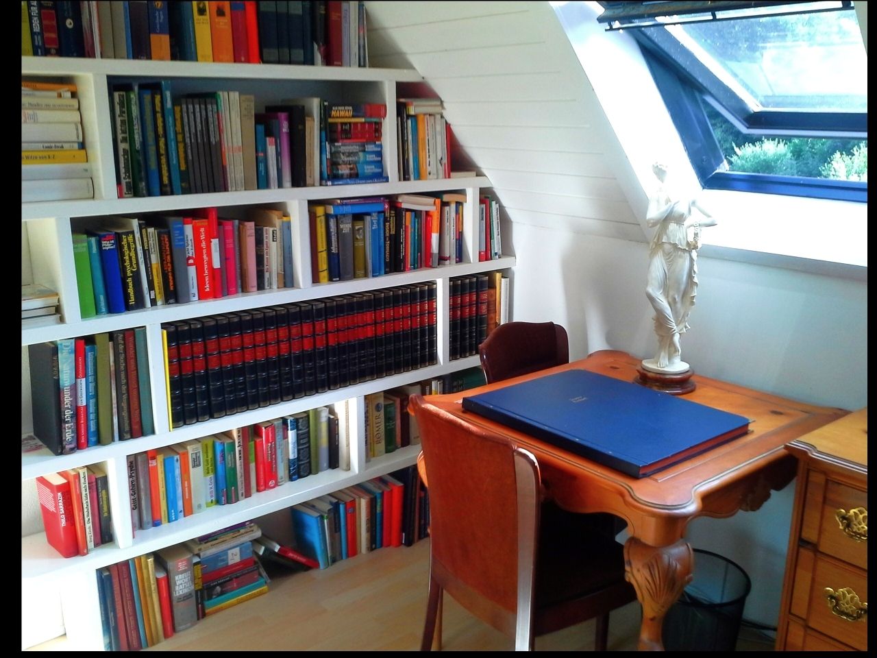 A cozy work area with bookshelf, desk and statue.