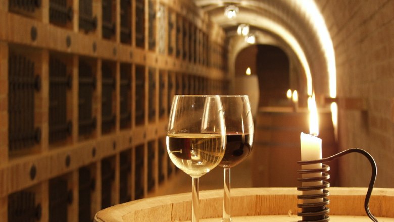 Two wine glasses and a candle on a barrel in a wine cellar.