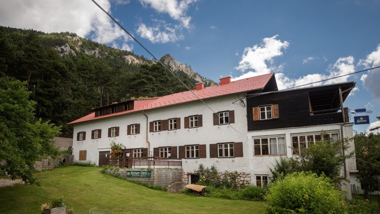 A traditional inn with a red roof in front of a wooded mountainside.