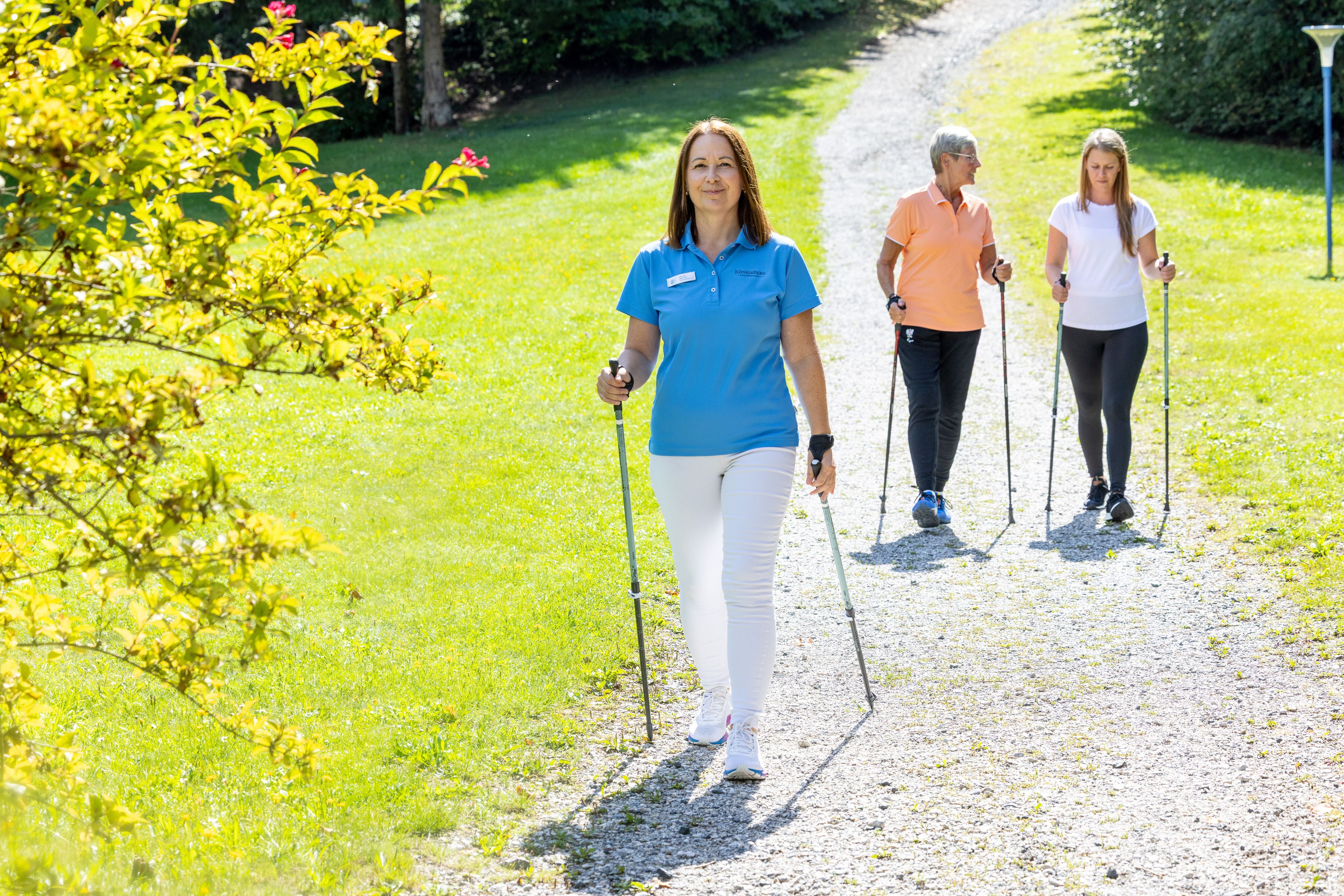Three women Nordic walking on a sunny path in the countryside.