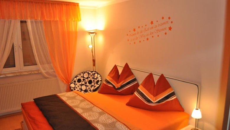 Cozy bedroom with orange bed linen and curtains, decorative cushions and wall tattoo.