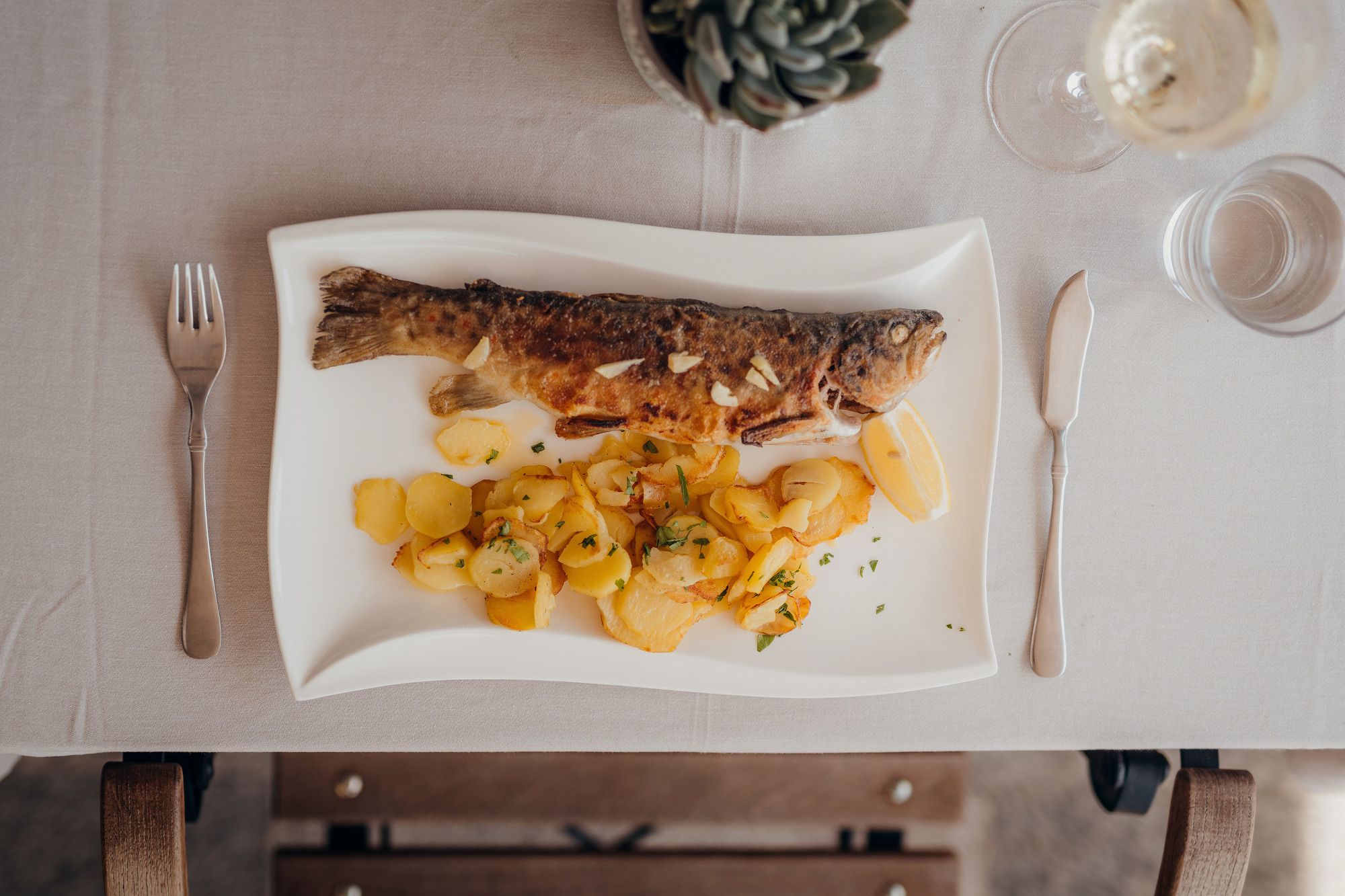 Trout with potatoes and lemon served on a white plate.