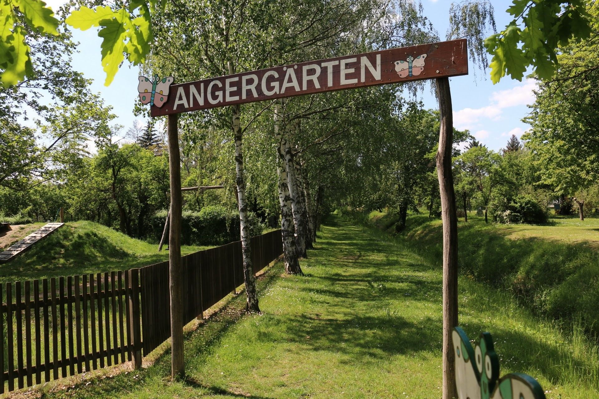 Entrance to the Angergärten with wooden sign and trees in the background.
