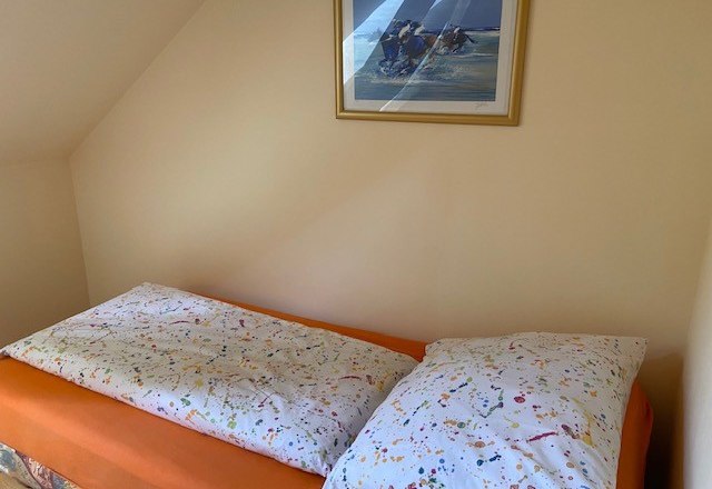A bed with colorful bed linen in a single room, with a framed picture on the wall above it.